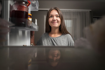 young woman looks into the fridge, view from fridge