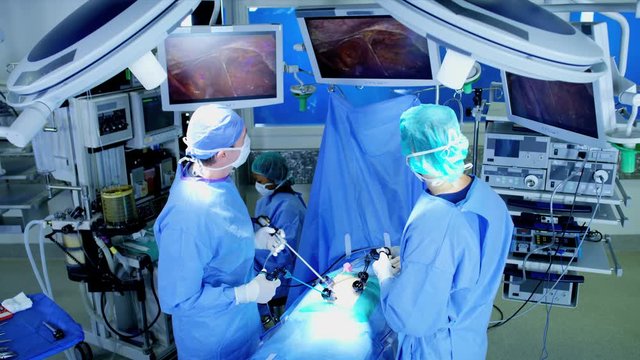 Laparoscopic surgical operation transmitted on hospital video monitors performed by Caucasian hospital surgeons wearing gloves and scrubs 
