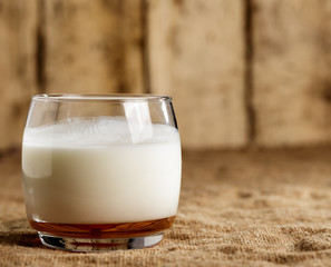 A glass of kefir stands on a burlap on the background of old boards.