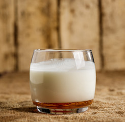 A glass of kefir stands on a burlap on the background of old boards.