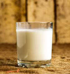 A glass of milk stands on a burlap on the background of old boards.