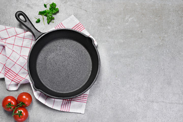 Cast iron pan on a grunge concrete background with copy space. Empty iron pan, top view or high angle shot with herbs and tomatoes.
