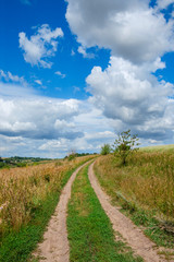 Sunny summer landscape with ground country road passing through the fields and green meadows.Beautiful white clouds in deep blue sky