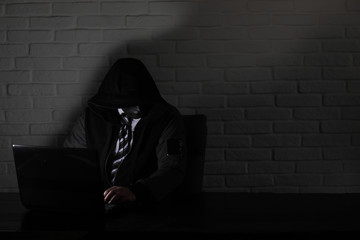 Hacker in black mask and hood at the table