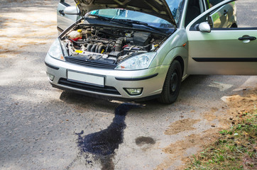 Broken car on the roadside with an open hood, trunk and doors. Oil leak from the engine on the asphalt