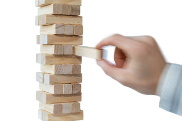 Man's hand taking first block or putting the last block to a sturdy tower of wooden blocks. Concept photo of planning, taking risks and strategizing. Hand is in motion. Isolated on white background.