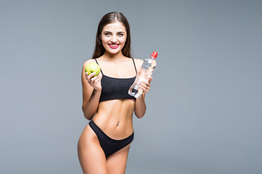 Young athletic girl holding a bottle of water and apple on a white background. Athletic woman on a white background