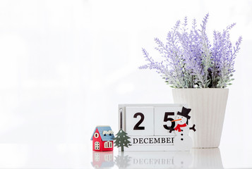 Cube wooden calendar showing date on 25 december with small wooden house, christmas tree ,houseplant and snowman on white table with vintage brick wall