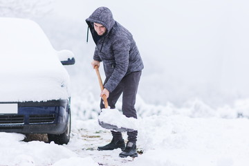 Man dressed in jacket cleaning snow around his car.