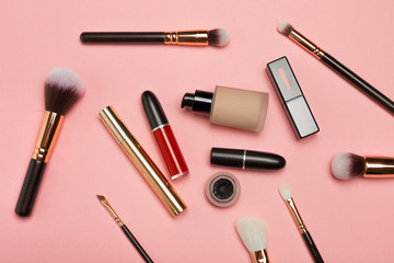 Professional makeup products with cosmetic beauty products, blushes, eye liner, eye lashes, brushes and tools on pink background