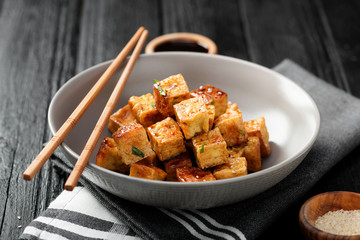 Fried tofu with sesame seeds and spices on black background.