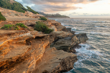 Waves Breaking into Makawehi Bluff while warm sunrise light illuminates the clouds, Kauai, Hawaii