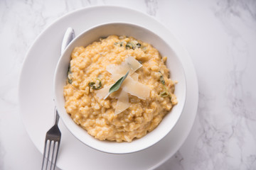 Pumpkin risotto with parmesan and sage. White marble background