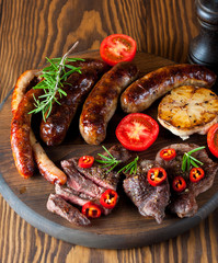 Close-up photo of mixed grilled meat platter. Beef, pork, poultry, sausages, grilled garlic, chili pepper, red tomatoes on wooden rustic background.