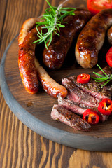 Close-up photo of mixed grilled meat platter. Beef, pork, poultry, sausages, grilled garlic, chili pepper, red tomatoes on wooden rustic background.