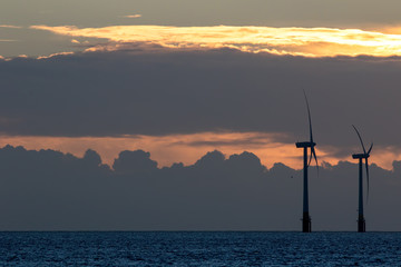 Offshore wind farm turbines silhouette at sunrise or sunset. Spiritual tranquil image conveying the future of green energy production.