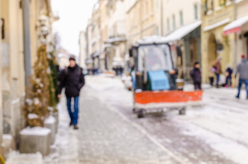 Blurred winter background city snow cleaner technician tractor removes snow communal services life bad weather lifestyle blizzard christmas cold falls snow tourists panorama old city