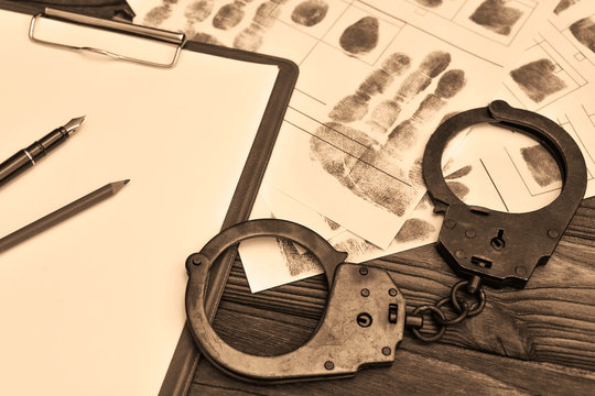 handcuffs, a blank sheet of paper, fingerprints on a wooden table background. arrest, detention of the criminal.