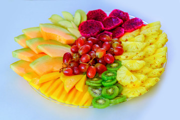Colorful, healthy foods great idea for good nutrition, vitamins gift for holidays. Fruit tray red pitaya dragon fruit, pineapple, grapes, mango, melon, kiwi on plate on white table.Flat lay, overhead.
