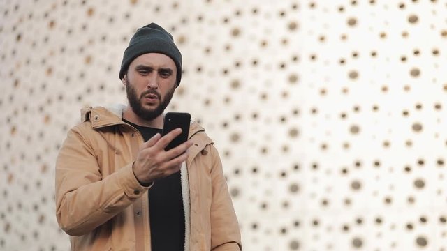 Young man reading bad news on smartphone standing near office center. he looks shockes and worried while checking news on smartphone. Lost businessman. Unsuccessful bet on the sport