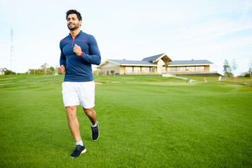 Active young athlete in sportswear jogging on green field in natural environment
