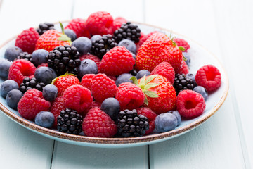 Fresh berry salad on blue dishes. Vintage wooden background.