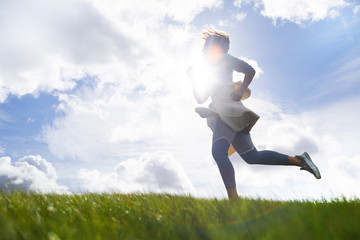 Active young woman jogging at skyline against sunshine on cloudy sky in natural environment