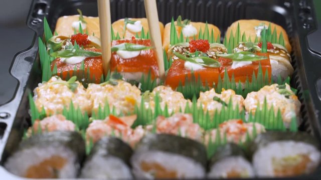 Top view on traditional japanese empty square black slate plate framed with sushi, ginger, soy, wasabi bowls, green leaves and chopsticks on rustic grey backround