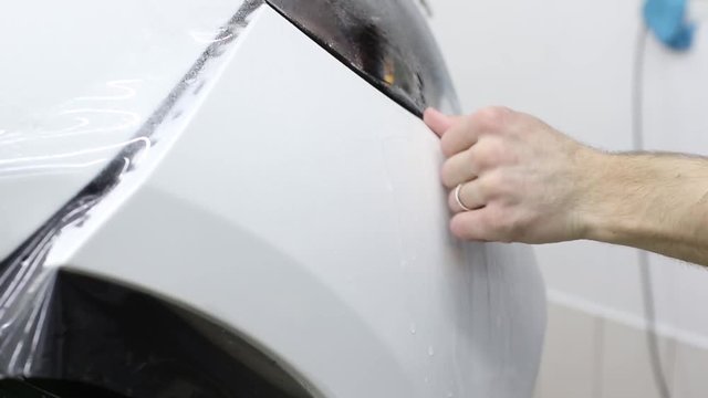 Close up shot of the hands of man who unstick the film with white cowl expensive car. This film protects the vehicle from the rough painting.