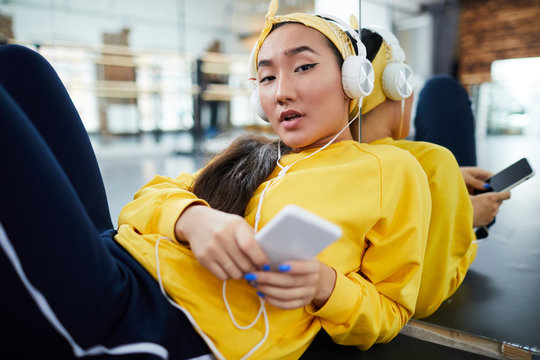 Active girl with smartphone listening to music in headphones during break between trainings