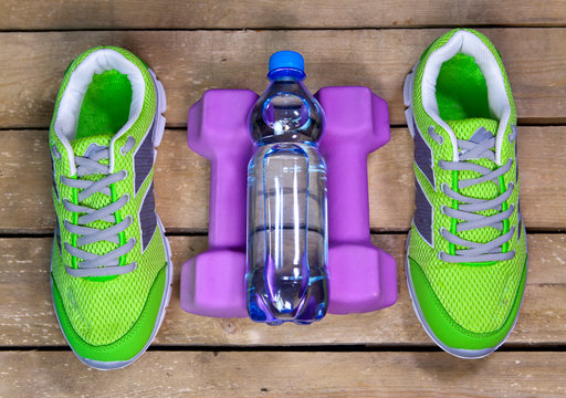 Sports sneakers, dumbbells, drinking water on a wooden background
