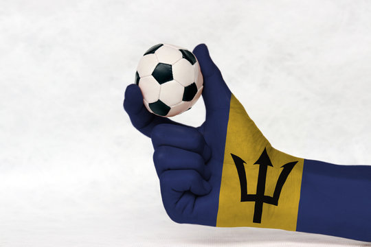 Mini ball of football in Barbados flag painted hand, hold it with two finger on white background. Concept of sport or the game in handle or minor matter.