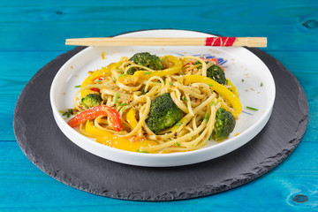 Asia food. Stir fry udon noodles with vegetables on a white plate, blue wooden backgound, cooked in wok