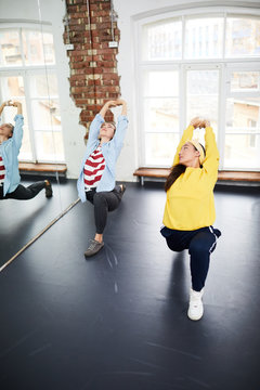 Two young flexible females in activewear doing hip hop exercise by large mirror in studio of dancing
