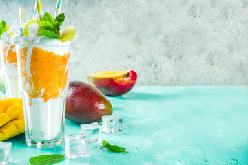 Tropical sweet dessert drink. mango milkshake or smoothie cocktail, with mango slices, mint and ice cubes, light blue background copy space