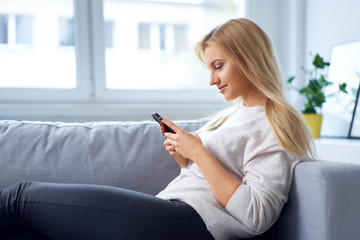 Smiling woman relaxing on sofa at home using smartphone