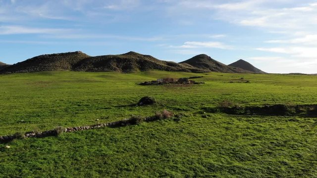 Cortijo abandonado en una bonita pradera verde. Preciosa ladera cubierta de hierba con monta&ntilde;as de fondo. Vista a&eacute;rea. Drone video 4k.