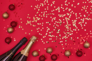 Two Champagne bottle with Christmas ornaments on red background. Copy space, top view, flat lay