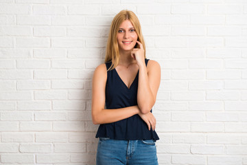 Blonde woman smiling and looking to the front with confident face on white brick wall background