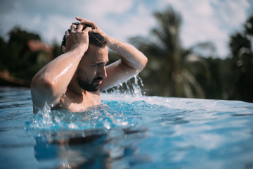 Portrait of a young handsome man in an outdoor pool. Attractive guy with a beard at the side of the pool
