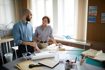 Two young professional tailors consulting about items of their new seasonal collection