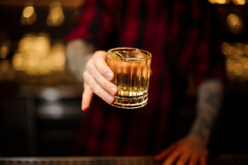 Tattooed bartender holding a cocktail glass with whiskey