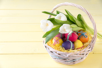 Basket with Easter eggs and flowers (white tulips) on a yellow table