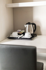 Tray with a kettle and white cups on the table. Hotel room