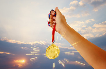 Fototapeta na wymiar woman hand raised, holding gold medal against sky. award and victory concept.