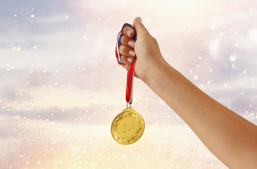 Obraz na płótnie Canvas woman hand raised, holding gold medal against glitter background. award and victory concept.