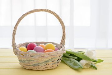 Basket with Easter eggs and flowers (white tulips) on a yellow table