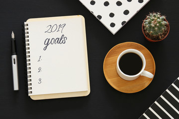 Fototapeta na wymiar Top view 2019 goals list with notebook, cup of coffee over wooden black desk.