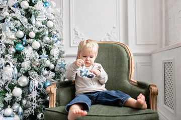 Portrait little boy. Happy new year. decorated Christmas tree. Christmas morning in bright living room. sitting on green chair