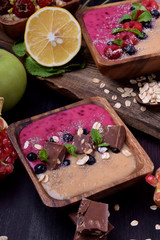 Smoothie bowl of two colours topped with chocolate pieces, bilberries, oatmeal flakes, mint and bran